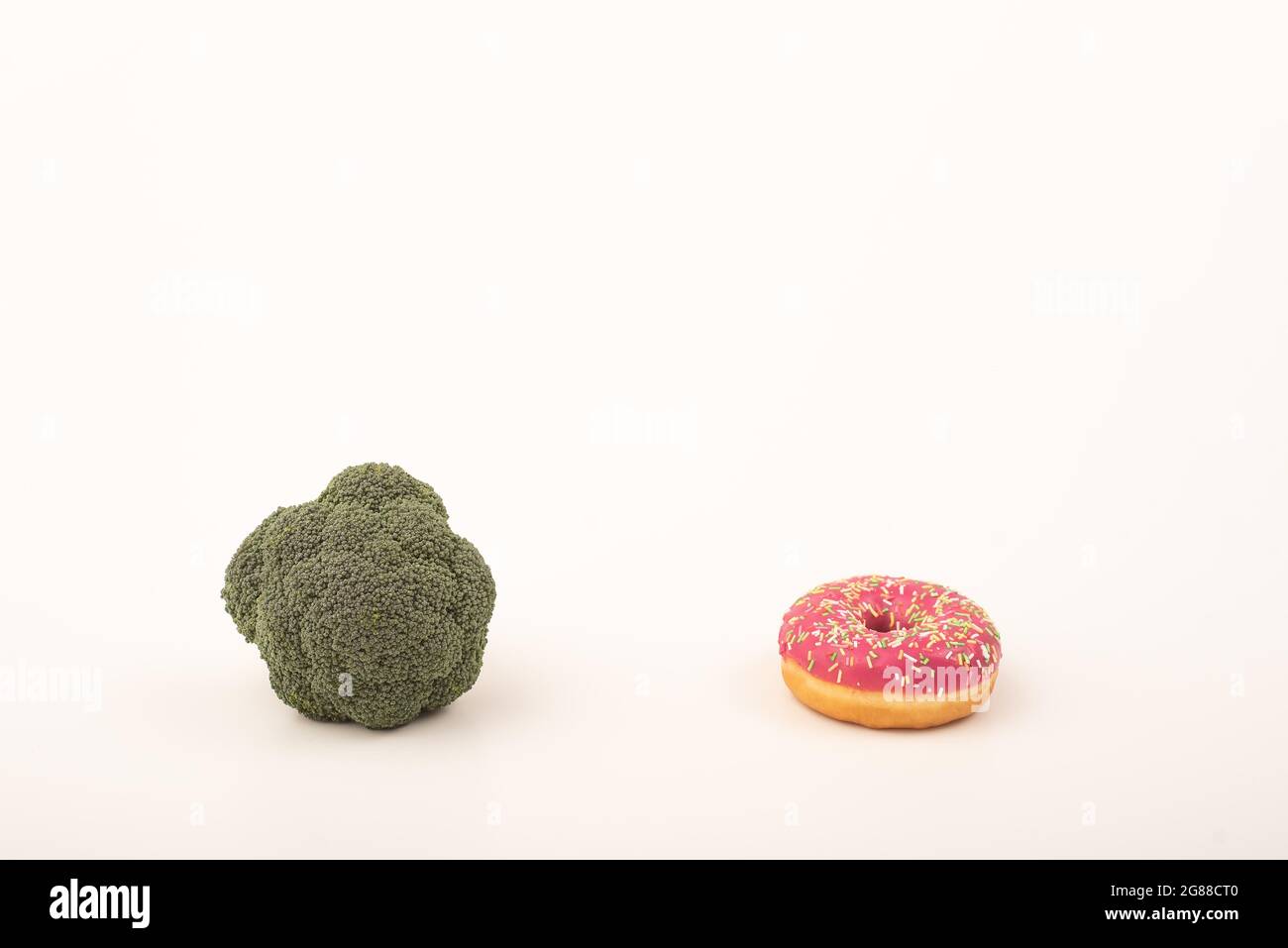 Confronto delle abitudini alimentari. Broccoli e ciambelle su sfondo bianco. Spazio di copia Foto Stock
