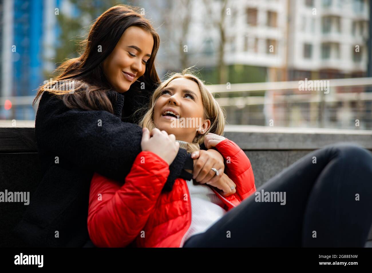 Primo piano di Happy Best Friends che si abbracciano e si siedono a terra Foto Stock