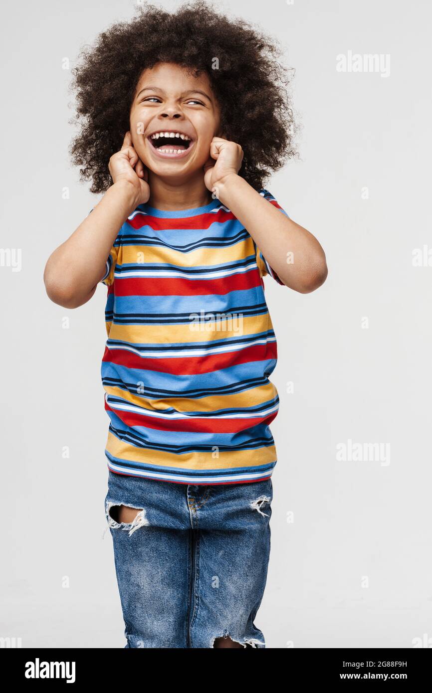 Sorridente ragazzo africano in abiti quotidiani sullo sfondo della parete, coprire le orecchie, gridare Foto Stock