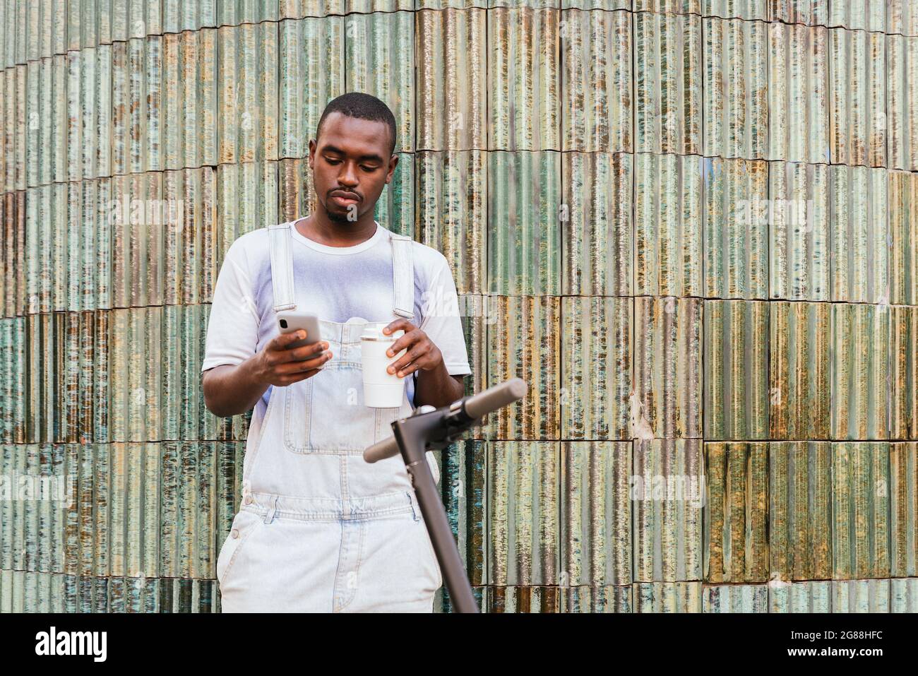 commuter africano maschio in piedi sulla strada vicino a uno scooter e utilizzando il suo telefono Foto Stock