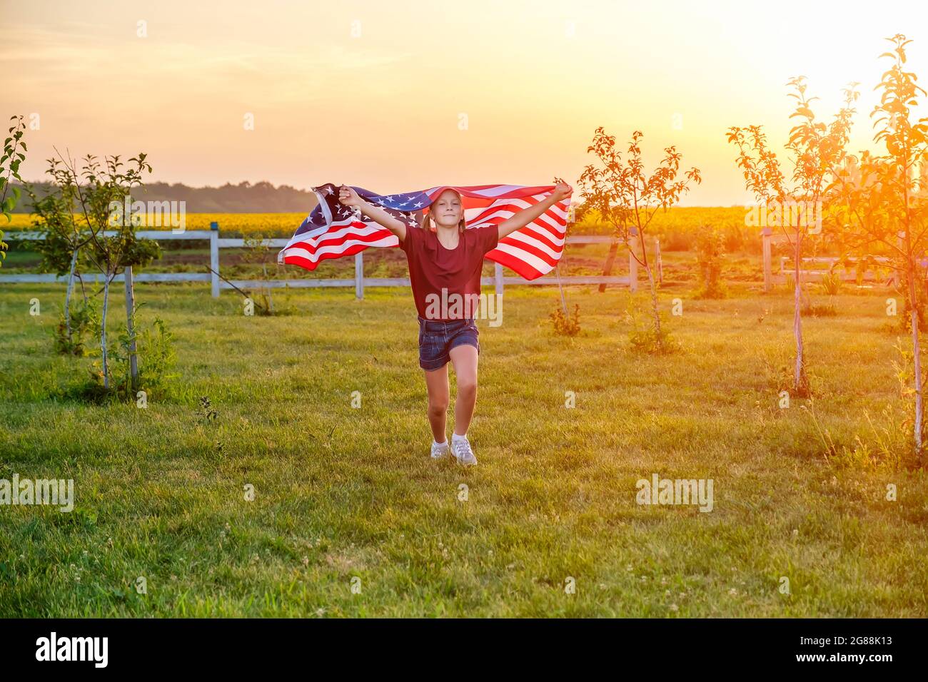 Bambino spensierato che corre in campo con bandiera americana soffiata in mani al tramonto Foto Stock