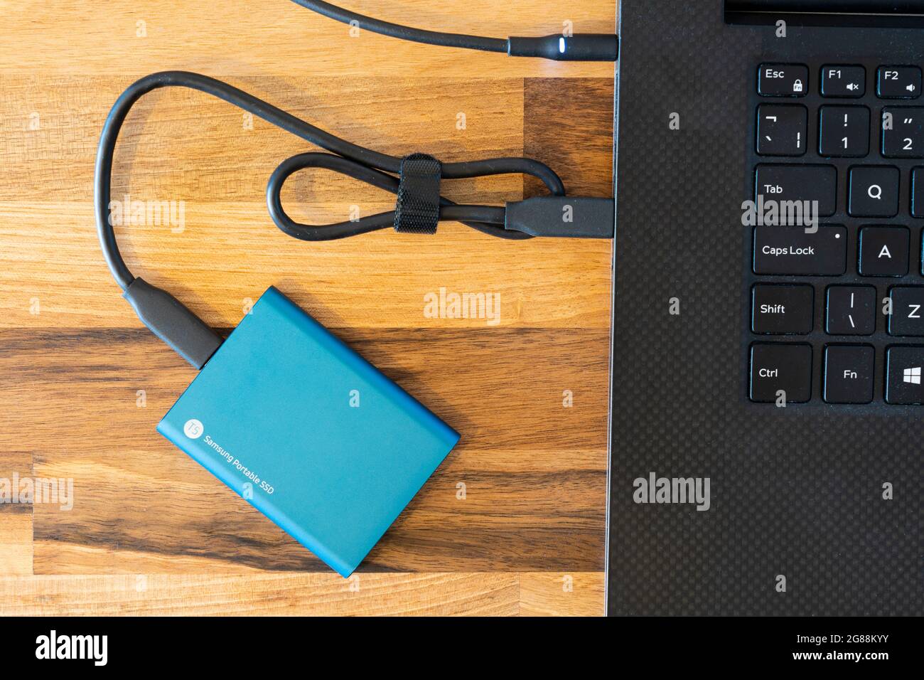 Un'unità portatile esterna SSD (Solid state Drive) crittografata da 500 GB Samsung blu per il backup dei dati con un cavo di connessione USB-C che lo collega a un computer portatile Foto Stock