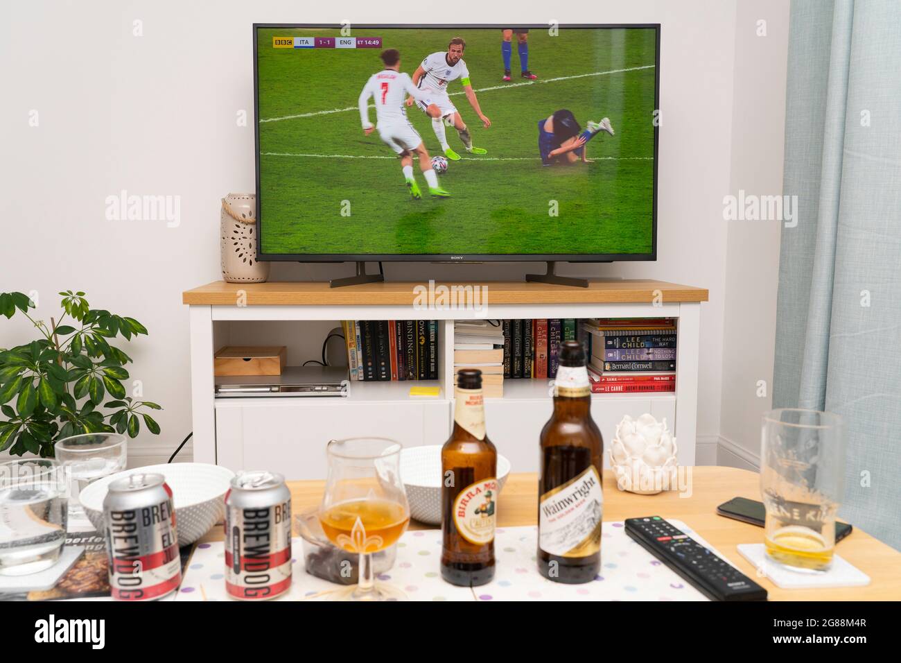 un televisore widescreen che mostra Harry Kane sulla palla durante la finale della competizione calcistica UEFA Euro 2020 con Inghilterra e Italia, con birre sul tavolo. REGNO UNITO Foto Stock