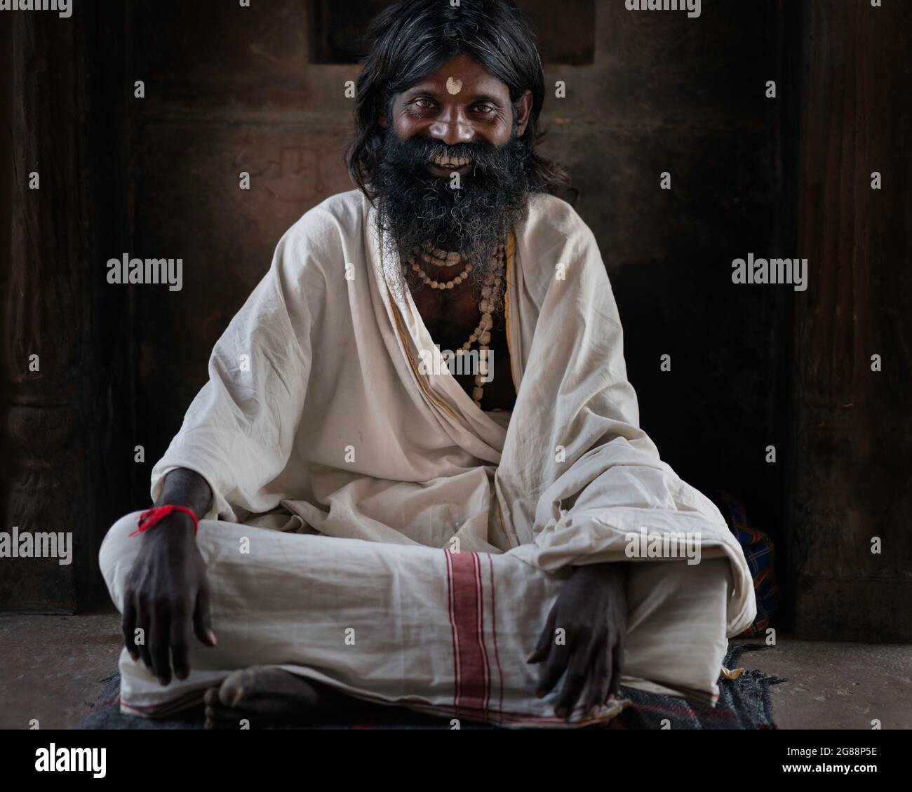 Ritratto di sadhu sorridente, uomo santo indù, con barba che scorre seduto nel tempio di Vrindavan, Uttar Pradesh, India. Foto Stock