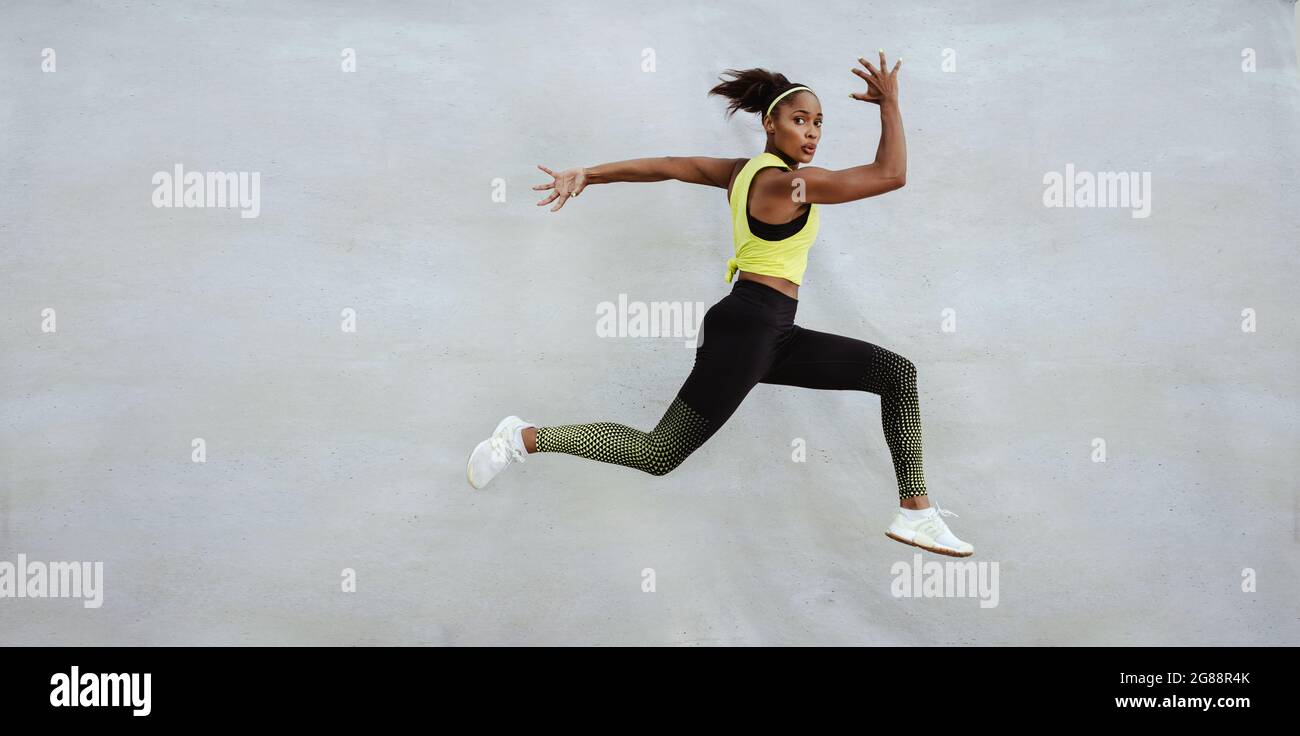 Donna runner sportiva su sfondo grigio. Vista laterale foto di donna in abbigliamento sportivo. Movimento dinamico. Sport e stile di vita sano Foto Stock