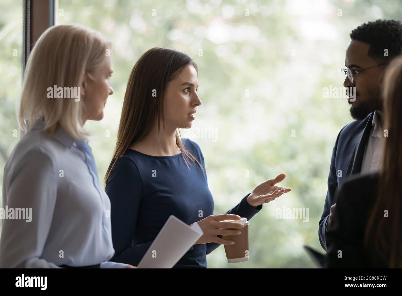 Un giovane dipendente serio che parla con colleghi diversi Foto Stock