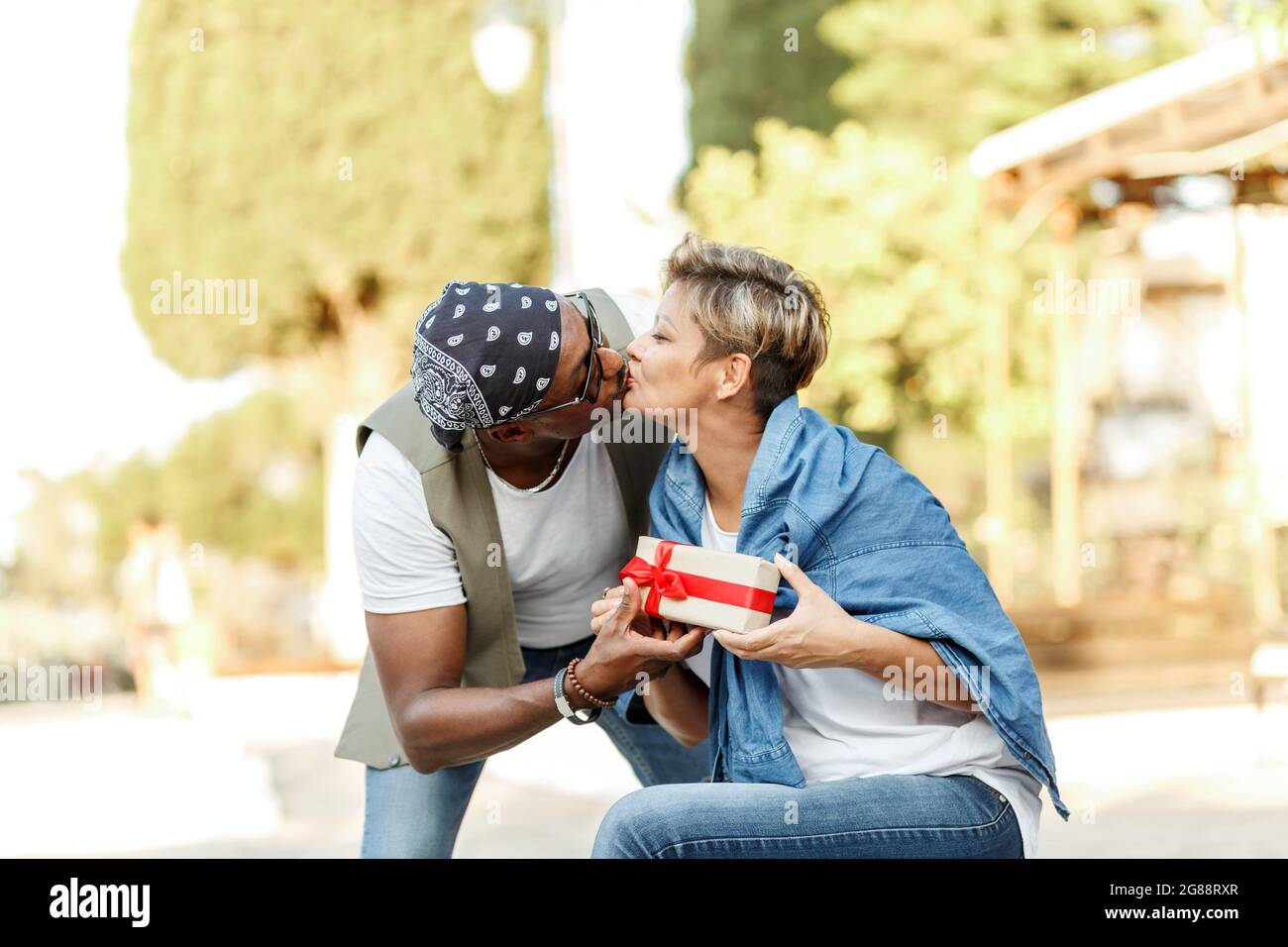 Felice coppia interracial di mezza età seduta . Uomo che dà il regalo di San Valentino alla sua donna, ragazza o moglie. Foto Stock