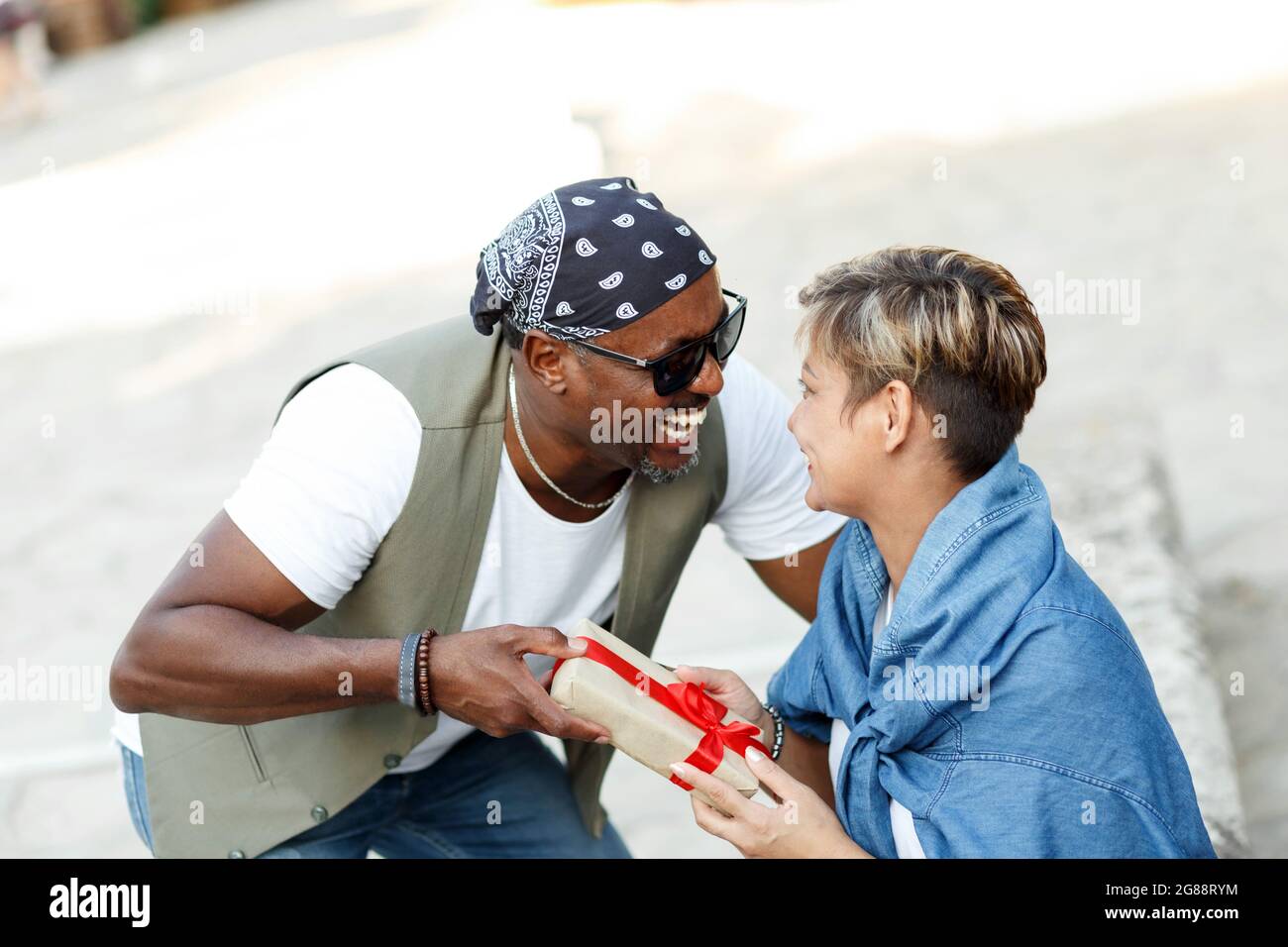 Felice coppia interracial di mezza età seduta . Uomo che dà il regalo di San Valentino alla sua donna, ragazza o moglie. Foto Stock