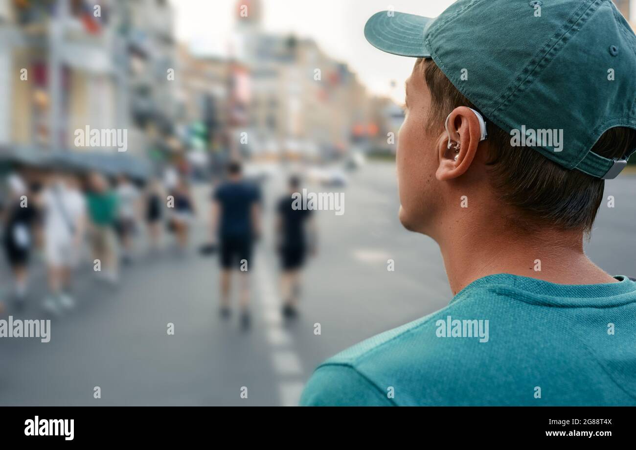 Vita umana con un apparecchio acustico. Un giovane con un apparecchio acustico dietro l'orecchio in una città rumorosa sente bene le persone intorno Foto Stock