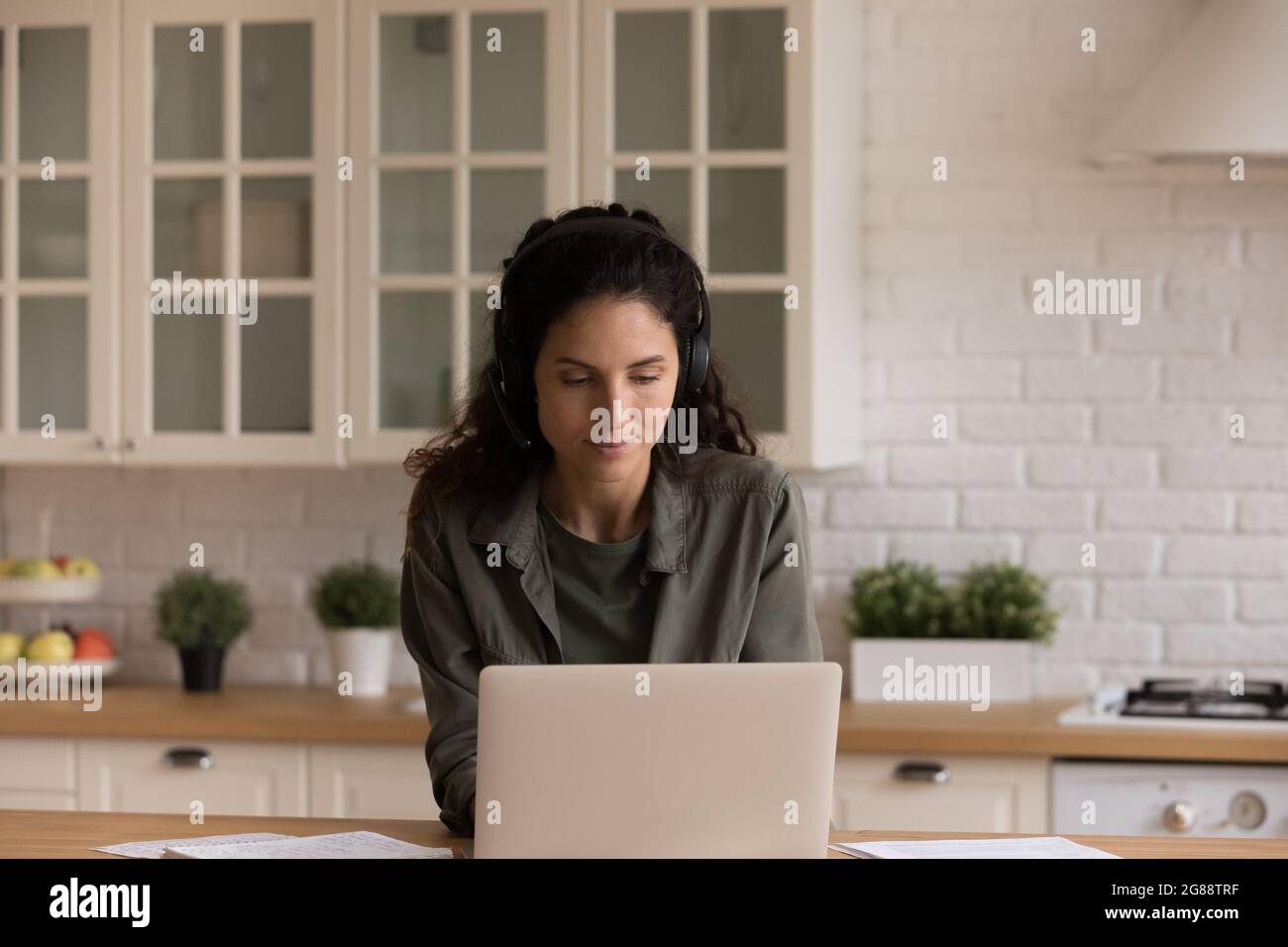 La giovane donna in cuffia lavora su un computer portatile dalla cucina di casa Foto Stock