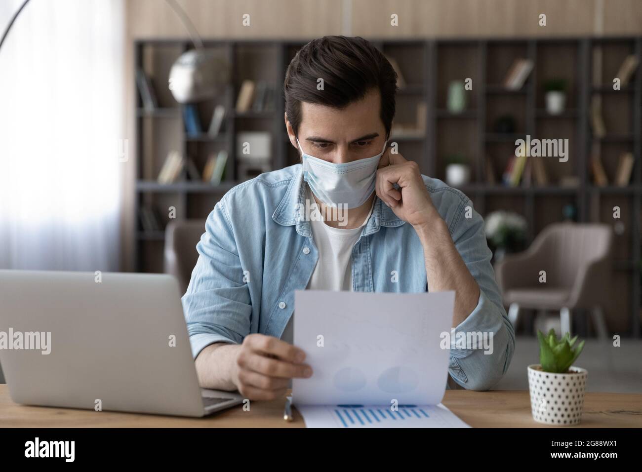 Dipendente maschile concentrato in facemask che lavora durante la pandemia di covid19. Foto Stock