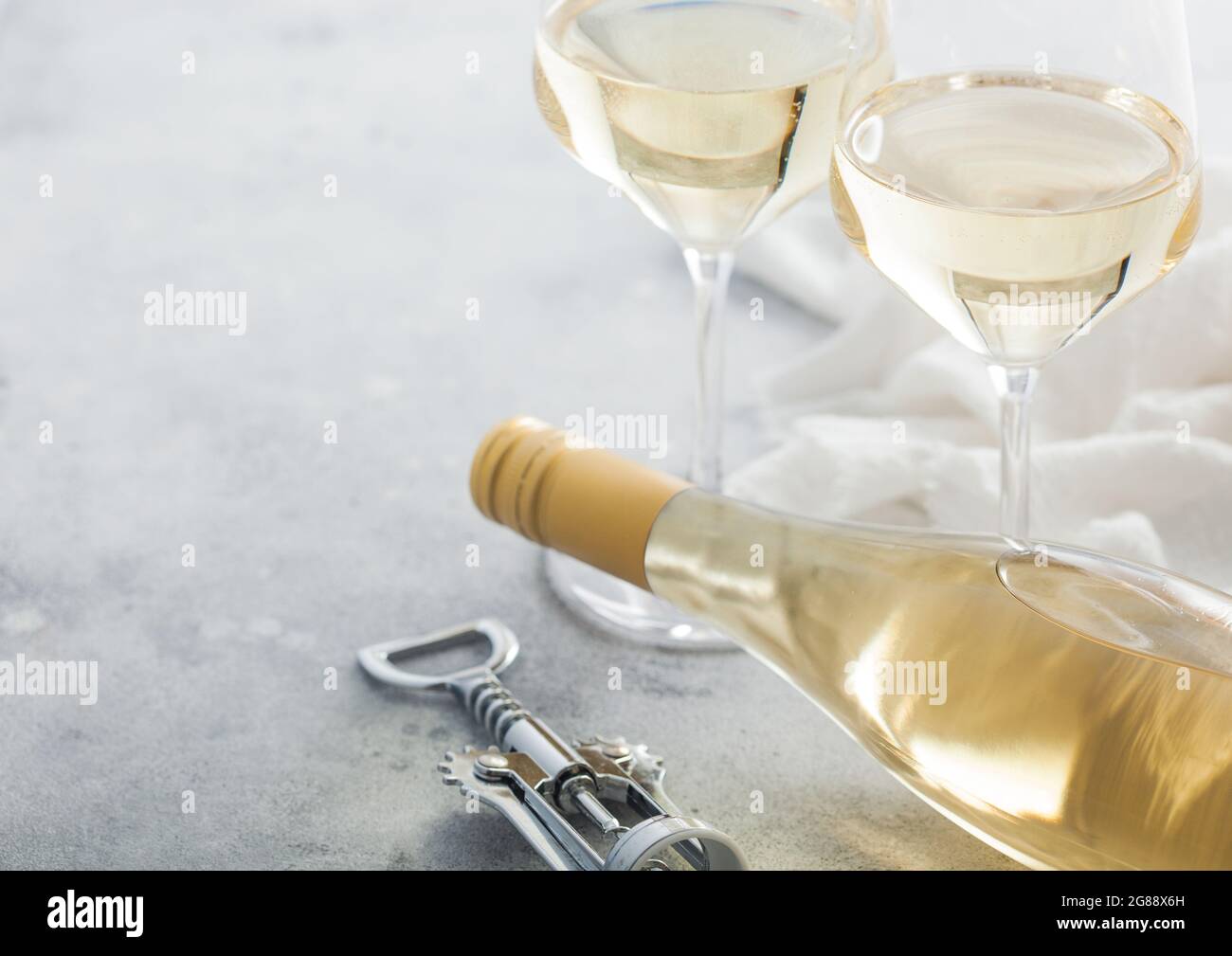 Due bicchieri di cristallo e una bottiglia di vino bianco fatto in casa con cavatappi in acciaio su sfondo chiaro. Spazio per il testo Foto Stock