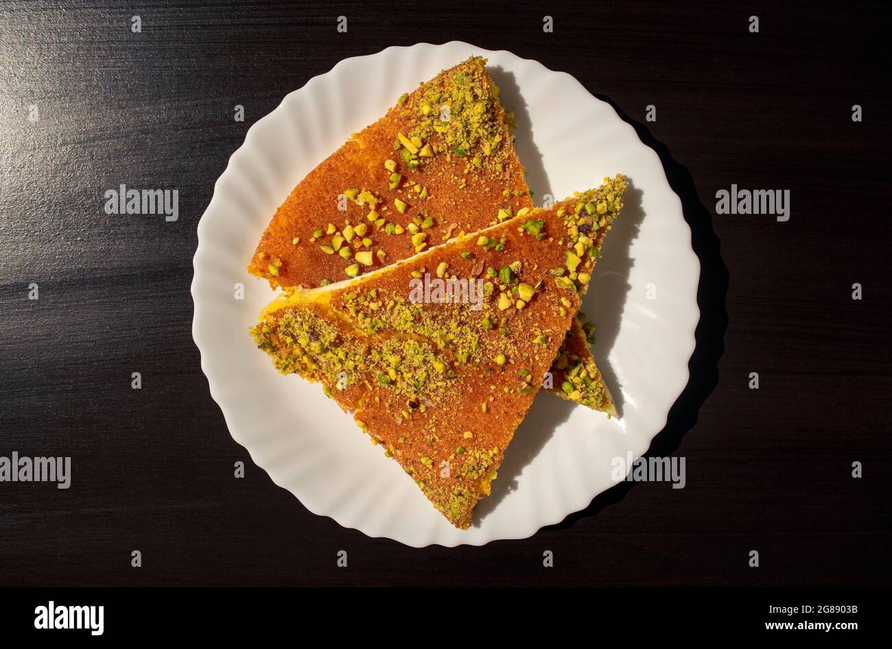 Fette di kunafa da dessert orientale su un piatto bianco su sfondo nero scuro. Vista dall'alto. Kunafa al formaggio arabo al buio. Foto Stock