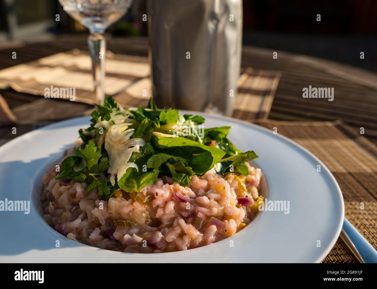 Pasto estivo all'aperto sotto il sole: Risotto a base di carne di granchio e cipolla rossa con finocchio rasato, basilico e prezzemolo, bicchiere di vino di cristallo e refrigeratore del vino Foto Stock