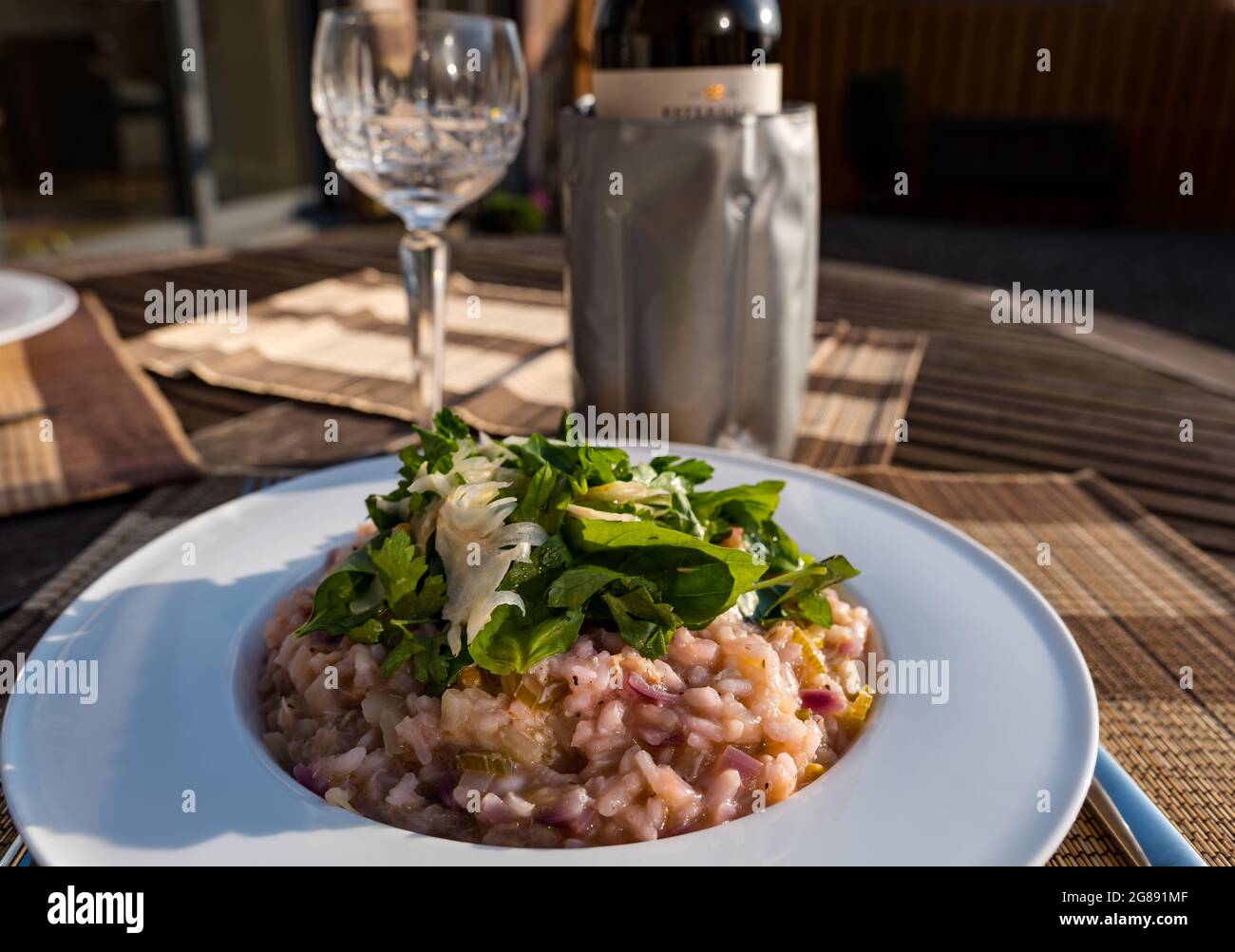 Pasto estivo all'aperto sotto il sole: Risotto a base di carne di granchio e cipolla rossa con finocchio rasato, basilico e prezzemolo, bicchiere di vino di cristallo e refrigeratore del vino Foto Stock