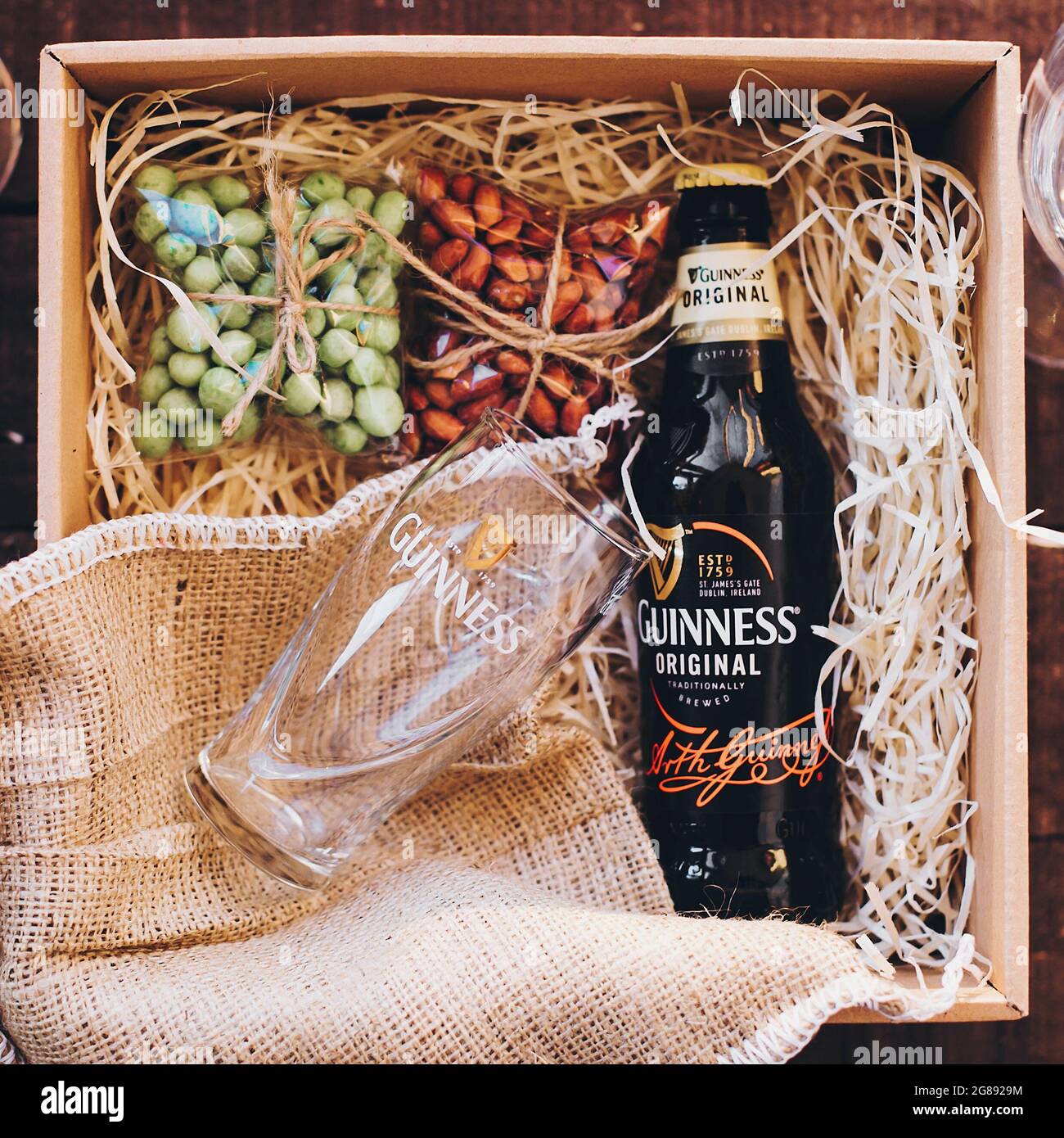Lviv, Ucraina - 1° dicembre 2017: Bottiglia di birra Guinness e bicchiere con etichetta e spuntini di noci salate sulla paglia in confezione regalo. Elegante confezione regalo per uomo Foto Stock