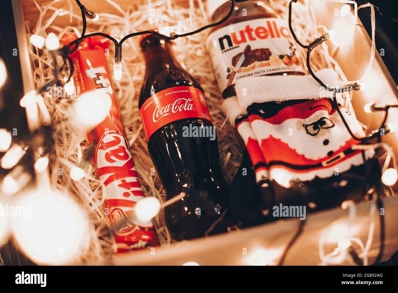 Lviv, Ucraina - 1 dicembre 2017: Bottiglia di Coca cola, calze babbo natale  eleganti, kat kit e nutella su paglia in scatola regalo con luci di natale.  Confezione regalo per Foto stock - Alamy