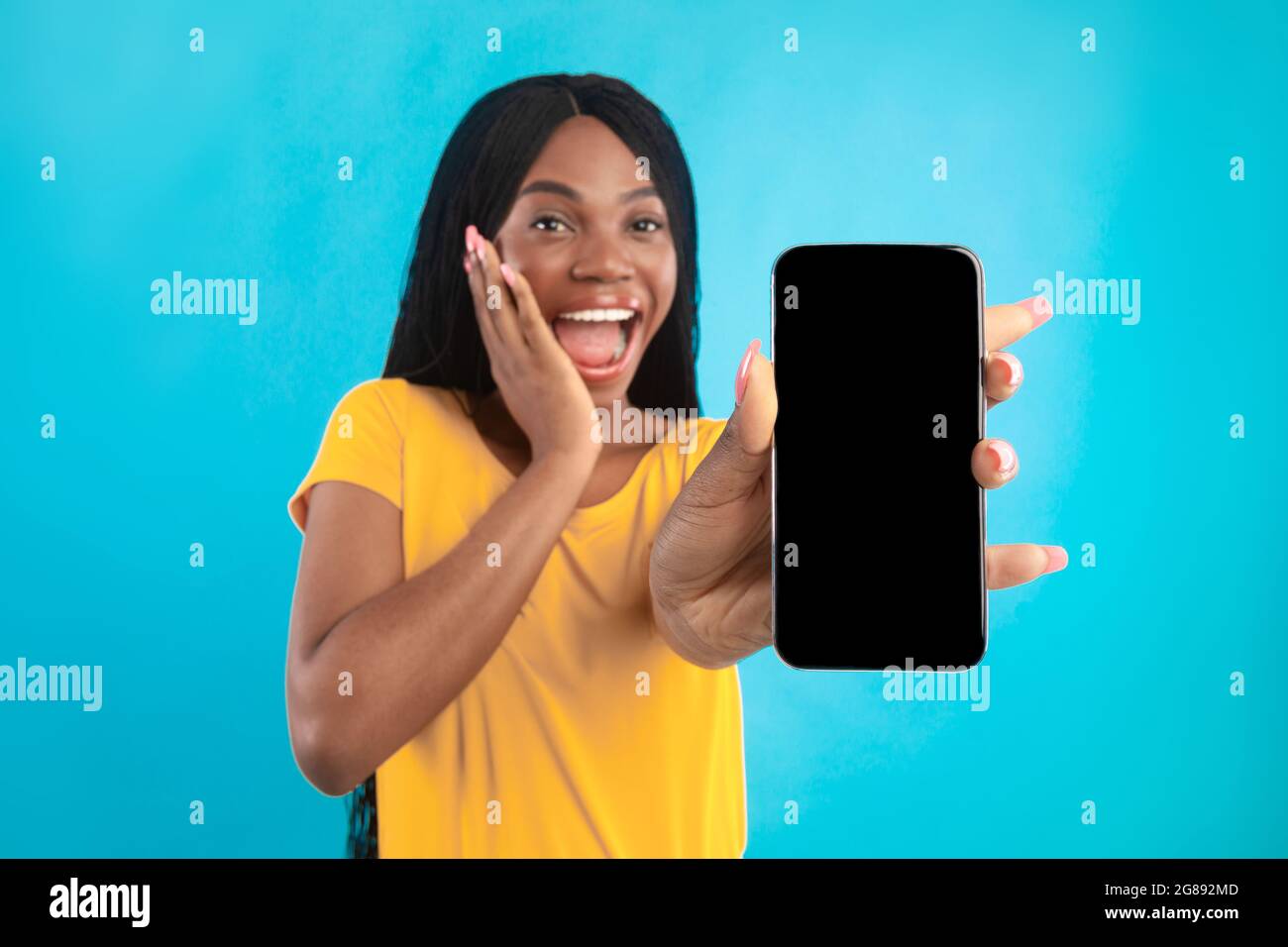 Eccitato African American Lady che mostra schermo del telefono su sfondo blu Foto Stock
