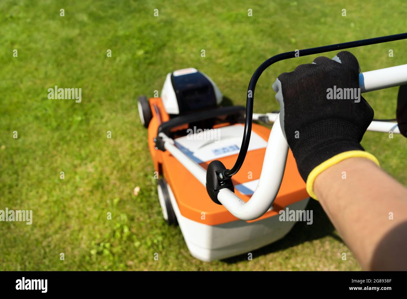 Una donna giardiniere sta rifilando l'erba con il tagliaerba e le mani in guanti Foto Stock