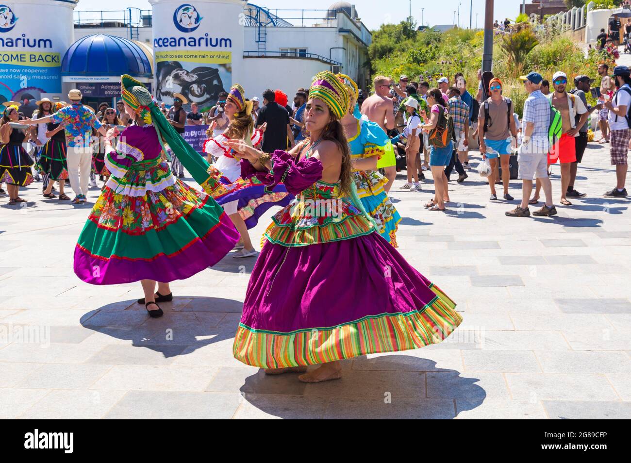 Bournemouth, Dorset, Regno Unito. 18 luglio 2021. Afon sistema con i loro ballerini strizzarri con gonne colorate giocano Maracatu, cugino Earthier di Samba del nord-est delle Brazilas si esibiscono come parte della serie estiva Arts by the Sea in una calda giornata di sole affollata sul mare. Credit: Carolyn Jenkins/Alamy Live News Foto Stock