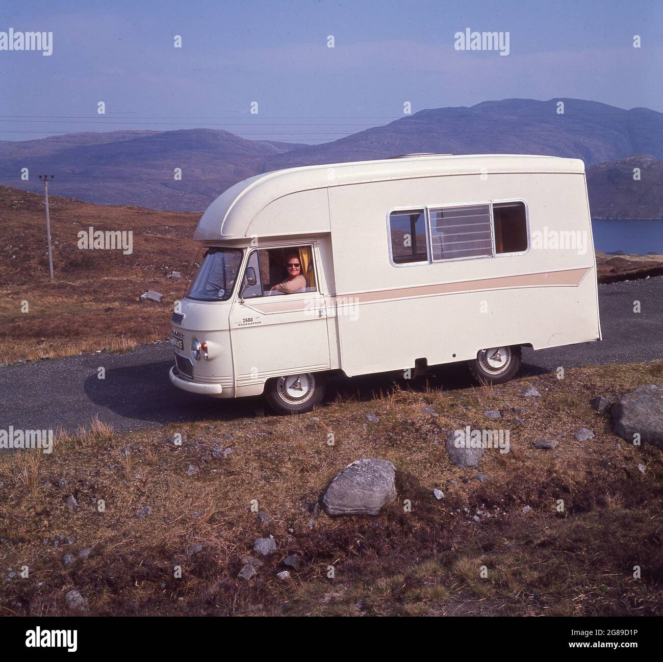 1970, storico, che visita le Highlands scozzesi, una signora seduta in un campervan Comper, una 'Jennings' 2500 Roadranger su una strada collinare sull'Isola di Harris, Highlands, Scozia, Regno Unito. Il Roadranger era un camper costruito in carrozza, la produzione è iniziata nel 1968, sviluppato dal Comcher FC. Commercial, azienda britannica produttrice di veicoli commerciali, ha iniziato nel 1905 con il nome di Commercial Cars Ltd. Nella storia a scacchi della produzione automobilistica britannica, Commers è stata portata da Humber nel 1926, Poi nel 1931, divenne un cedente del Gruppo Rootes e poi Chrysler nel 1967 e poi da Renault nel 1979. Foto Stock