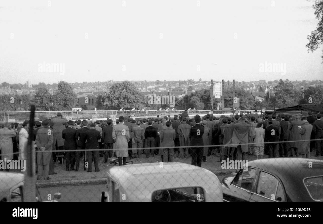 Anni '60, storico, vista su alcune auto parcheggiate di una folla di spettatori in un meetng di corse di cavalli, Inghilterra, Regno Unito. Foto Stock
