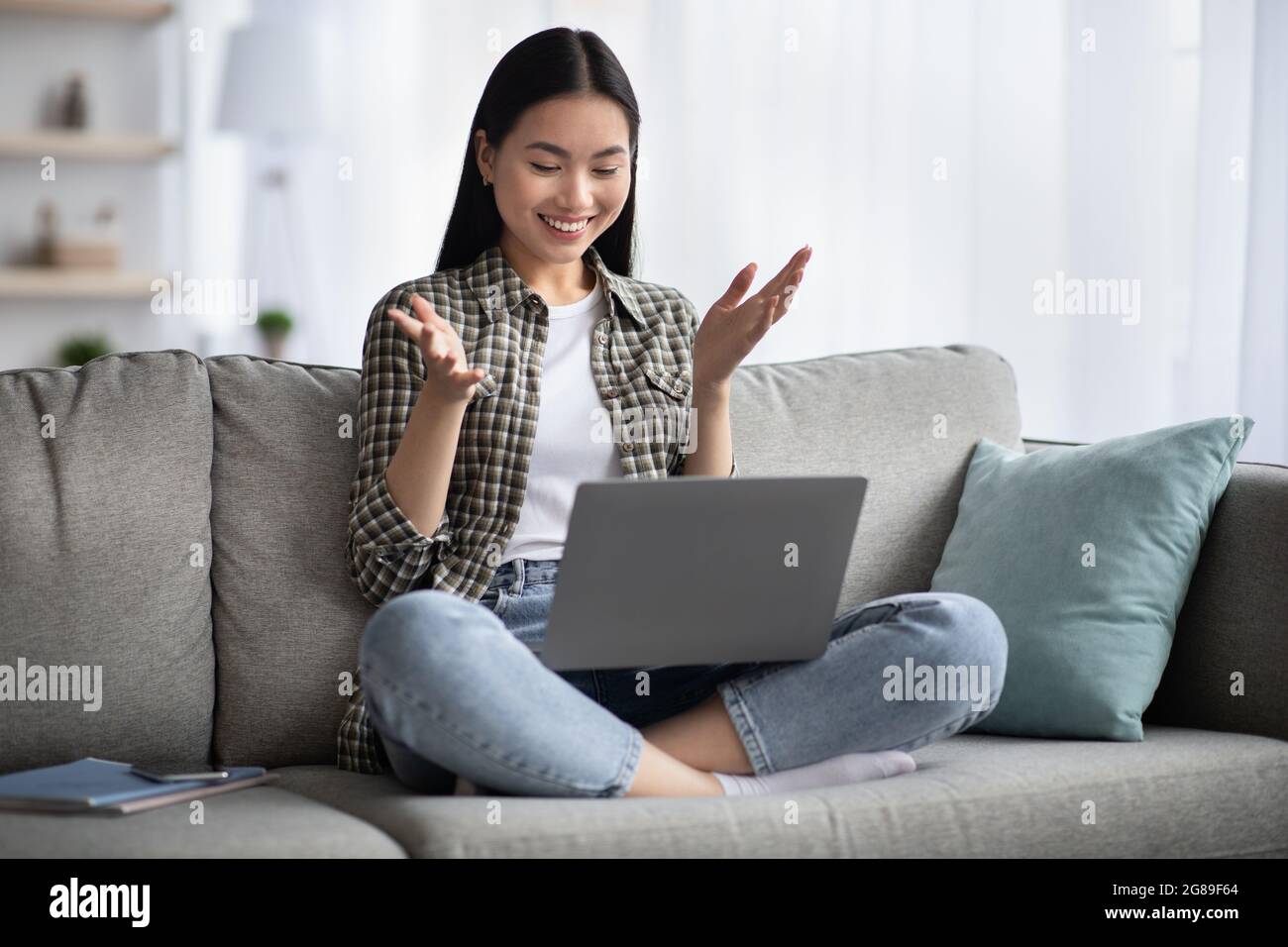 Bella giovane donna asiatica seduta sul divano con computer portatile Foto Stock