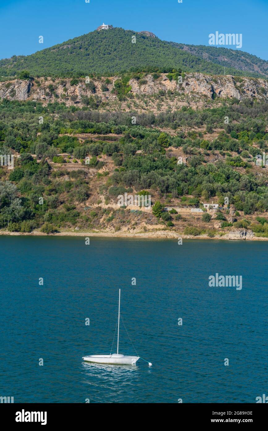 Piccola barca a vela ormeggiata a una boa nella diga di Beznar, Granada, con una montagna sullo sfondo e un eremo in cima. Foto Stock