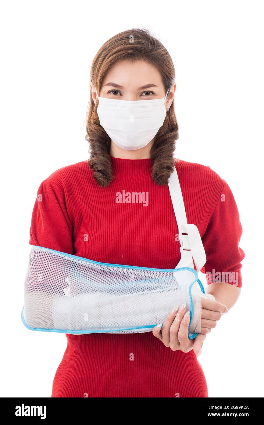 Bella donna asiatica con braccio rotto e bendaggio indossando maschera chirurgica di igiene protettiva in piedi isolato su sfondo bianco con faccia sorridente. INS Foto Stock