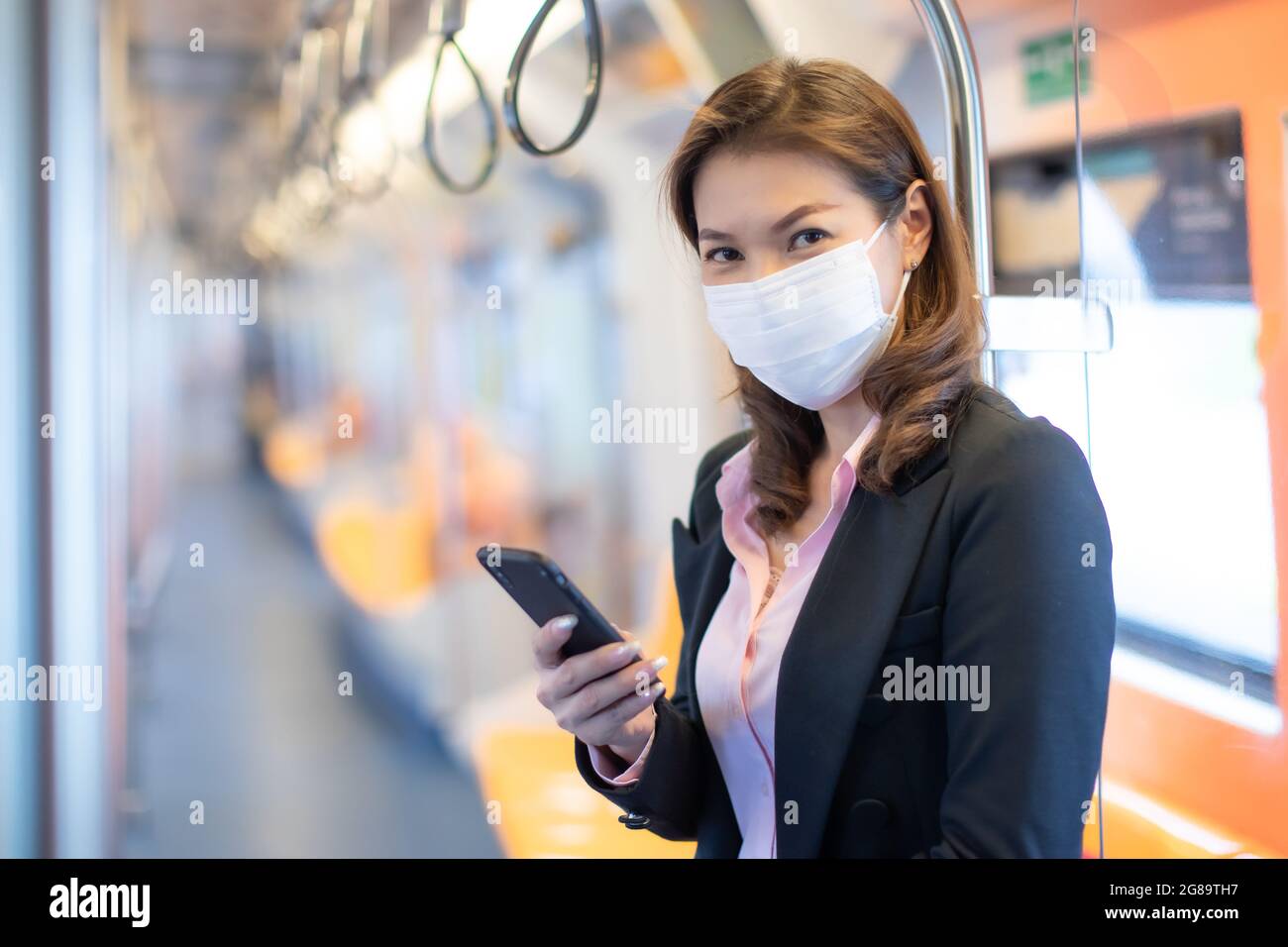 Bueatful adulto asiatico businesswoman passeggero commuter indossando maschera di protezione igiene medica. Stare in piedi e utilizzare il telefono cellulare all'interno della metropolitana vuota o del cielo Foto Stock