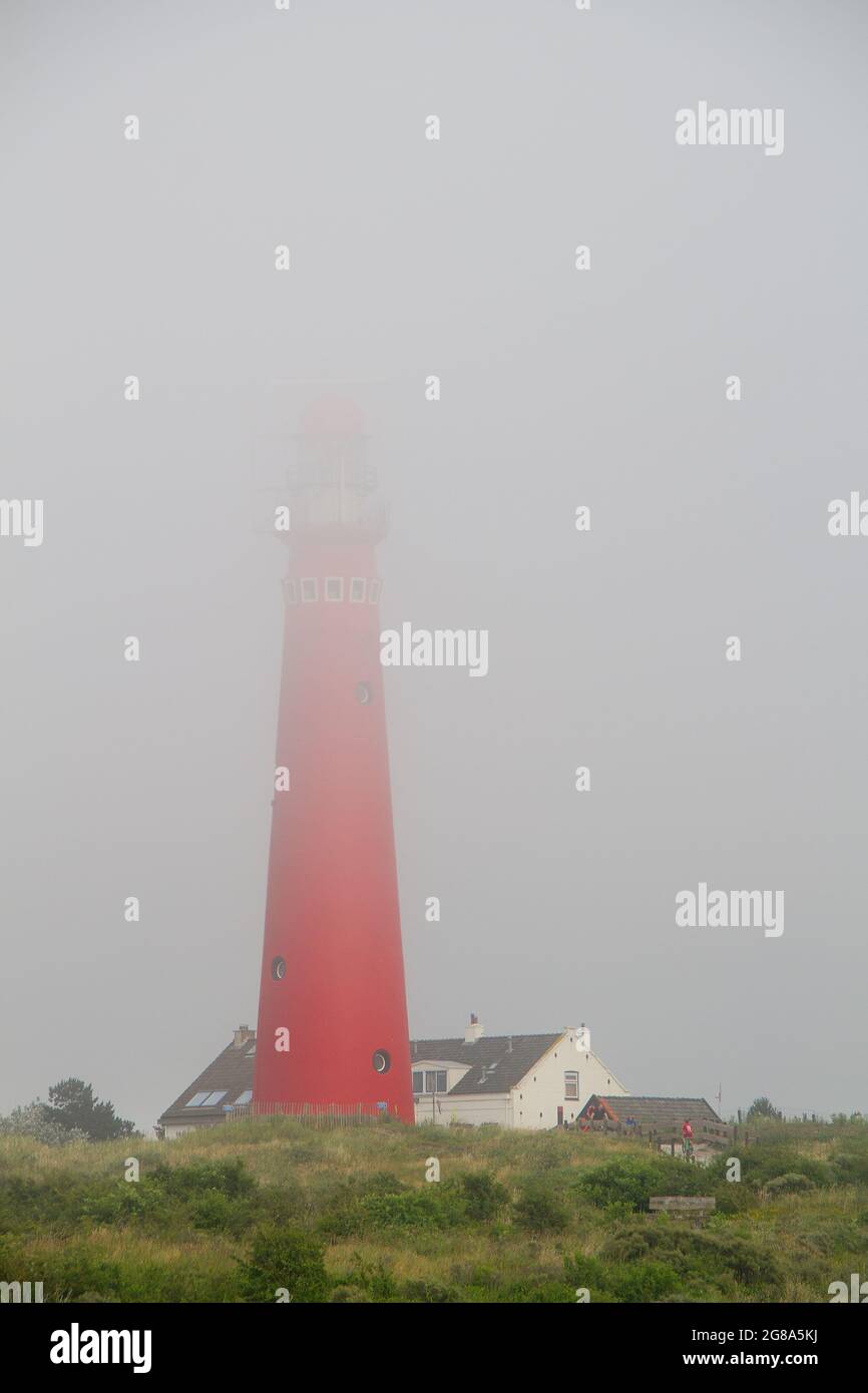 Faro rosso dell'isola olandese Schiermonnikoog in una giornata misteriosa, la cima del faro scompare nella nebbia. Foto Stock