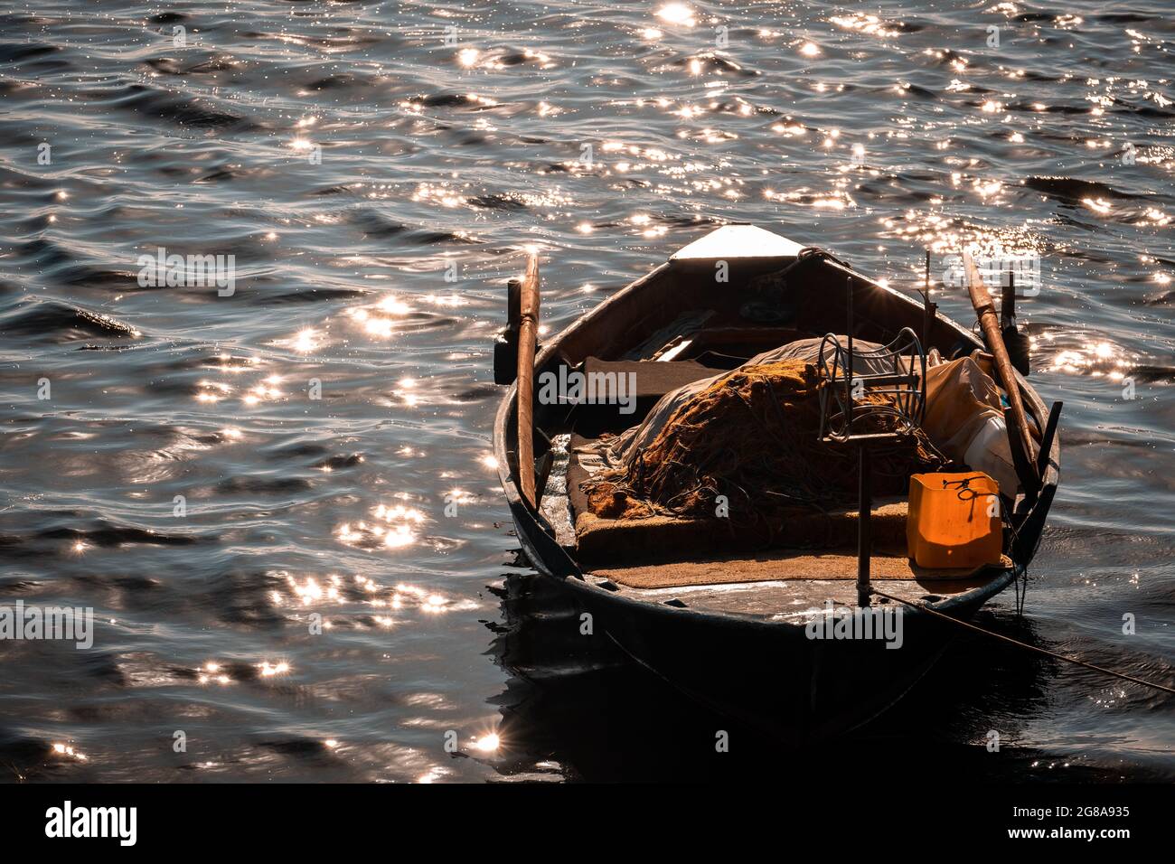 Piccola barca da pesca in mare in Grecia. Luce del mattino quasi alla luce del sole, raggio arancione sparso sul mare, con barca da pesca e frizzante surf in mare Foto Stock