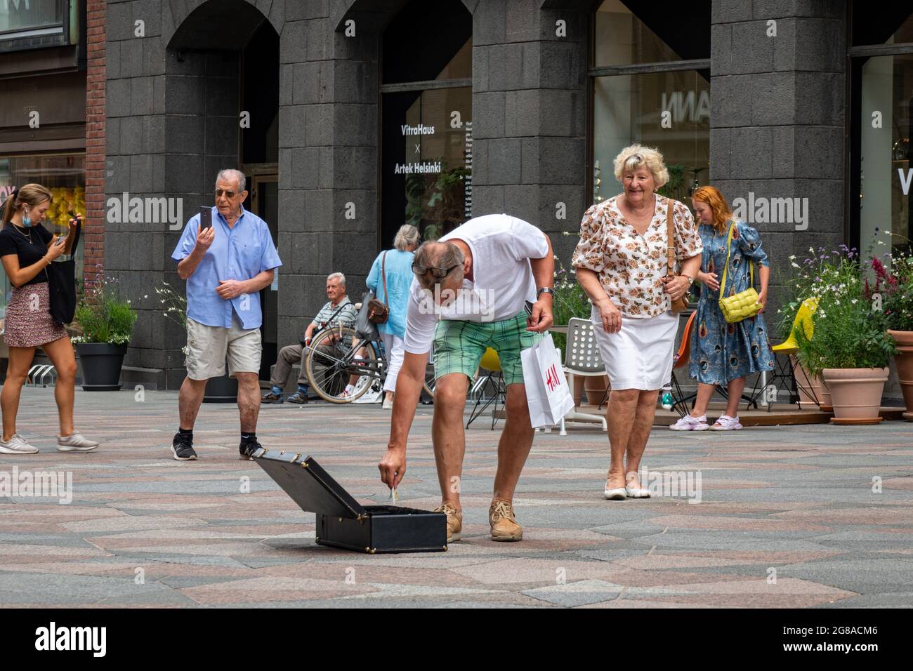 Uomo che fa cadere denaro nella valigia del busker di strada su Keskuskatu a Helsinki, Finlandia Foto Stock