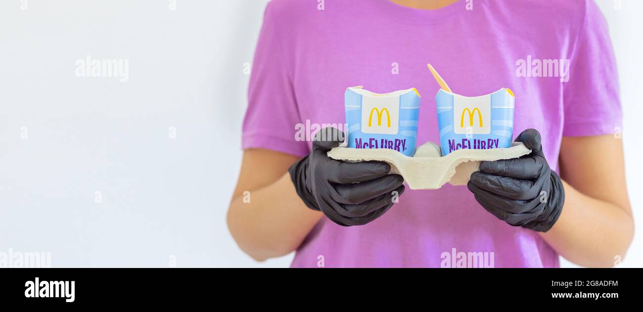 Donna in un t-short viola che tiene un gelato Mcflurry in guanti medici. Consegna McCafe. Fast food ristorante McDonalds. Gelateria via Foto Stock