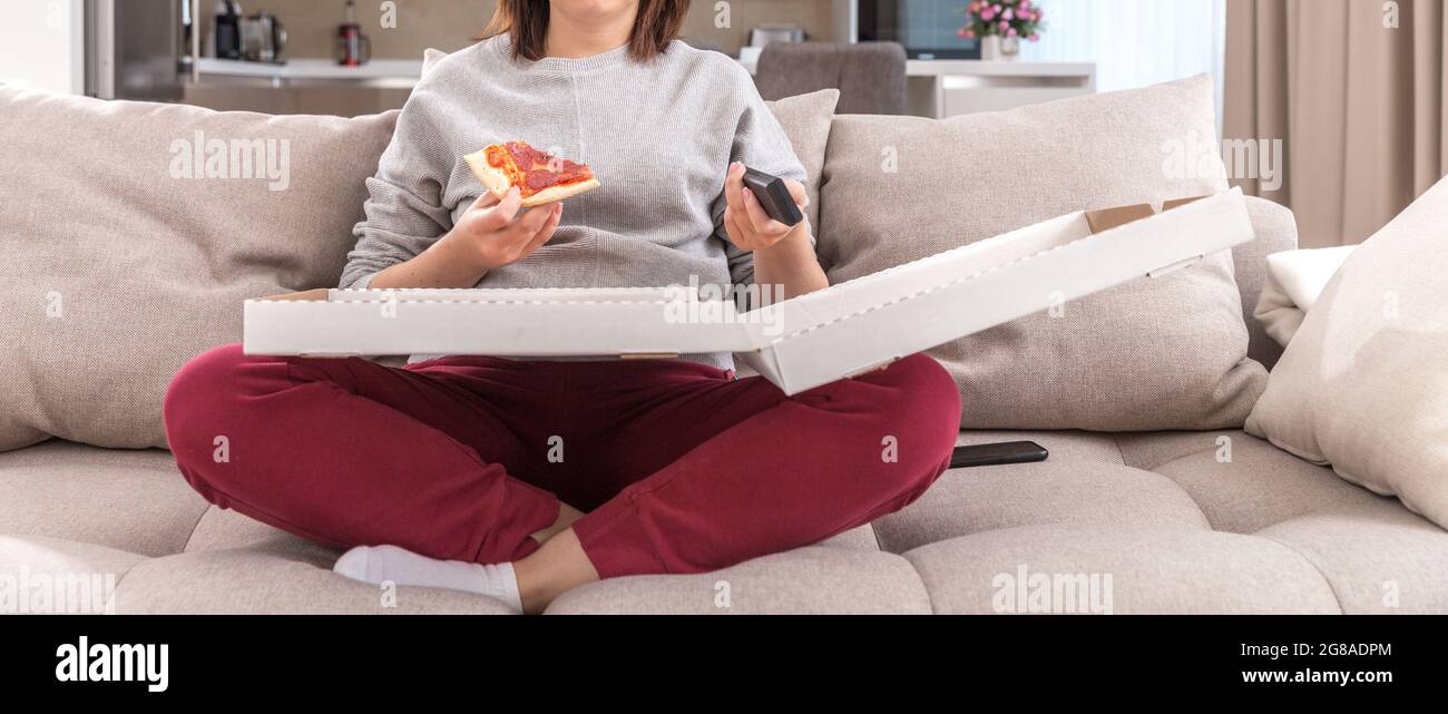 Ragazza che mangia la pizza seduto sul divano e guardando la tv in un appartamento moderno Foto Stock