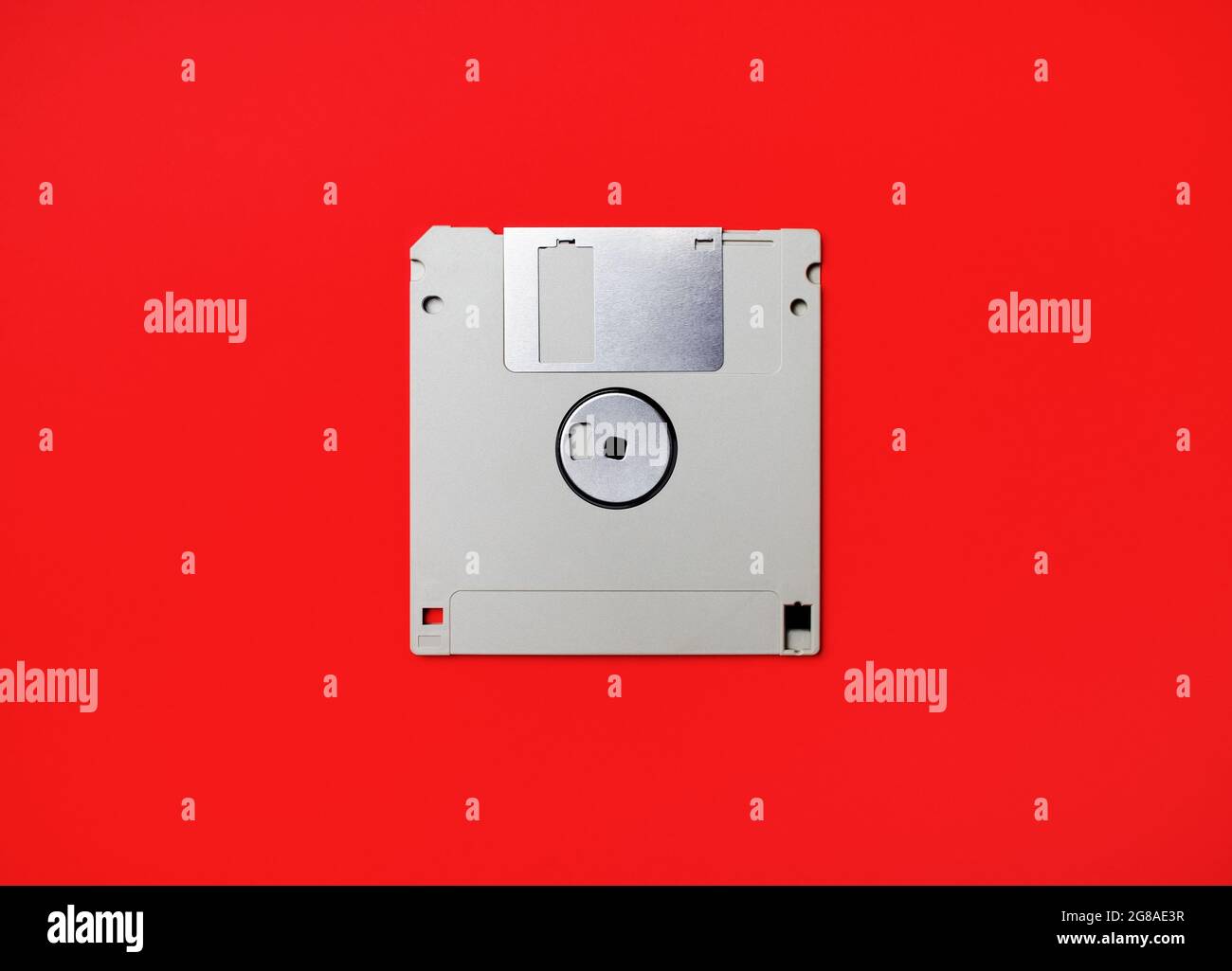 Dischetto grigio su sfondo di carta rosso. Disco floppy. Disposizione piatta. Foto Stock