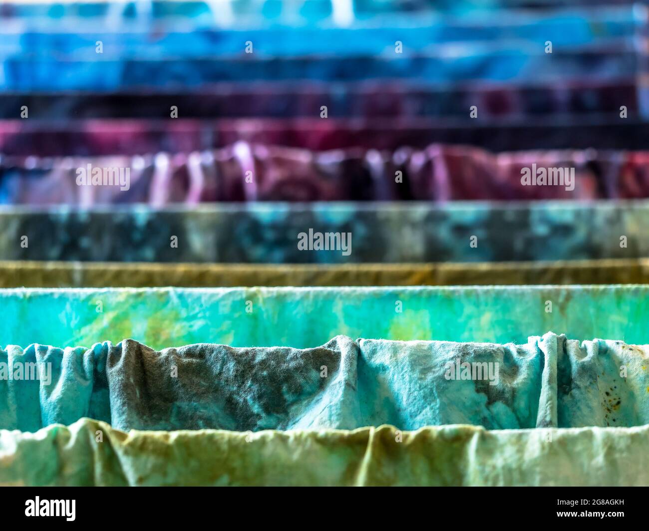 Closeup di vari colori tessuti di cotone umido tinti a mano che asciugano su un asciugatore Foto Stock