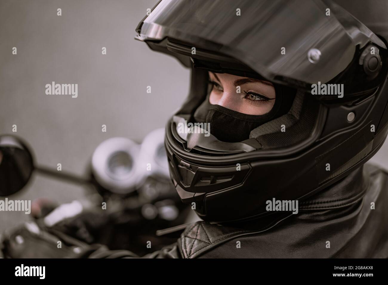 Donna motociclista elegante in casco e giacca in pelle seduta su moto nera. Driver femminile all'aperto su sfondo naturale. Viaggi, caffè racers Foto Stock