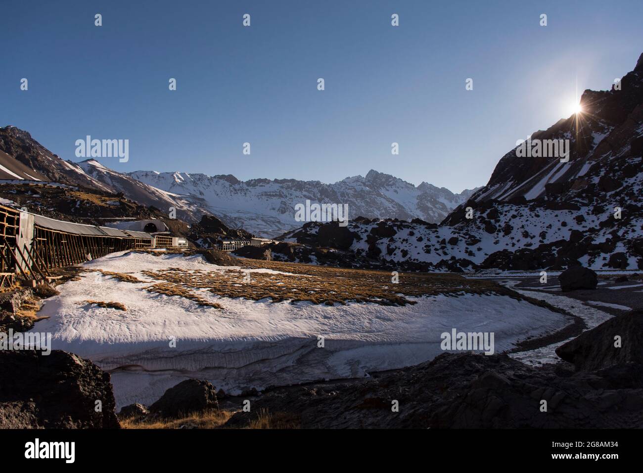 Paesaggio montano con neve nelle Ande con il sole all'orizzonte e una vecchia linea ferroviaria non in uso. Foto Stock