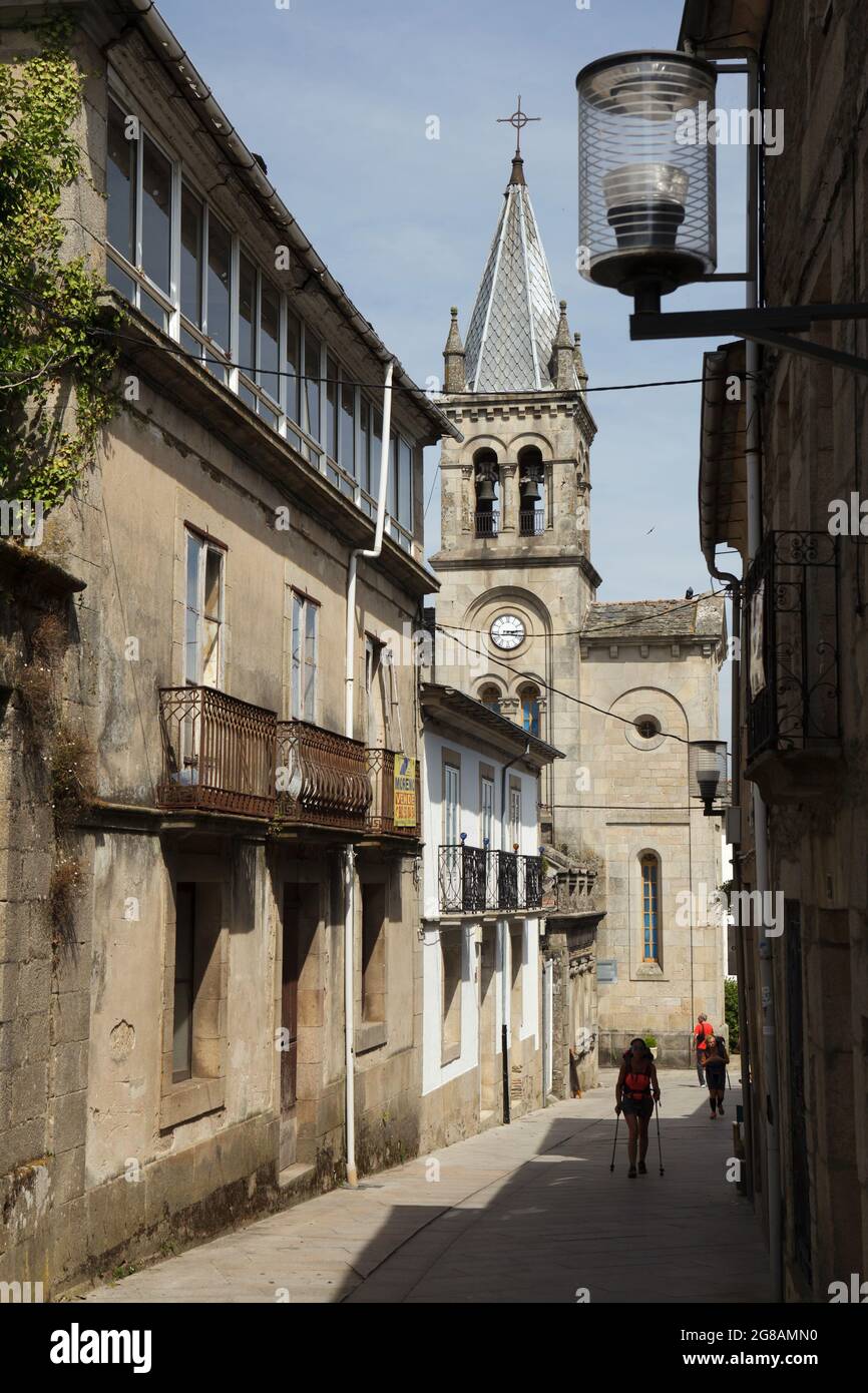 Camino de Santiago (Via di San Giacomo). I pellegrini camminano attraverso il centro di Sarria in Galizia, Spagna. La Chiesa di San Marina (Iglesia de Santa Mariña de Sarria) completata nel 1885 è visto sullo sfondo. Sarria è la città più popolosa sulla rotta francese del Camino de Santiago in Galizia. Foto Stock