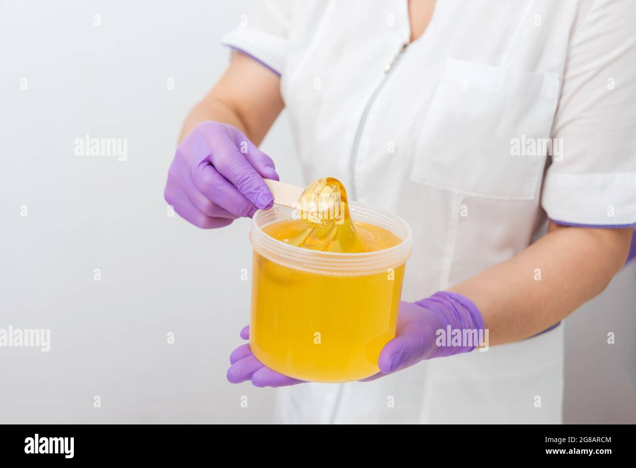 Pasta di zucchero al miele naturale, spugnante primo piano. Donne estetista tiene cera barattolo di pasta per la depilazione dello zucchero shugaring, fondo bianco Foto Stock