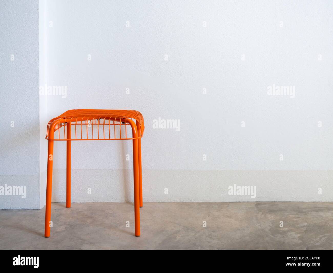 Sedia vuota fai da te colore arancione in acciaio e filo su pavimento in cemento e sfondo bianco parete con spazio copia. Moderna sedia con griglia geometrica wi Foto Stock