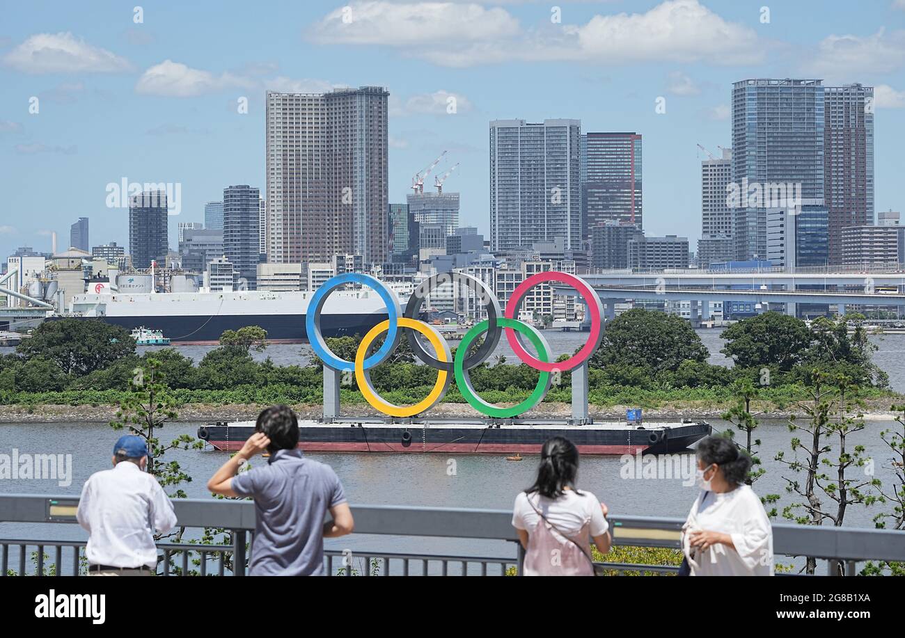 Tokio, Giappone. 18 luglio 2021. La gente si trova su una baia di fronte agli Olimpiadi di grandi dimensioni. Gli anelli si ergono su un pontile nella Baia di Tokyo di fronte al quartiere di Odaiba. Le Olimpiadi di Tokyo 2020 si terranno dal 23 luglio 2021 all'8 agosto 2021. Credit: Michael Kappeler/dpa/Alamy Live News Foto Stock