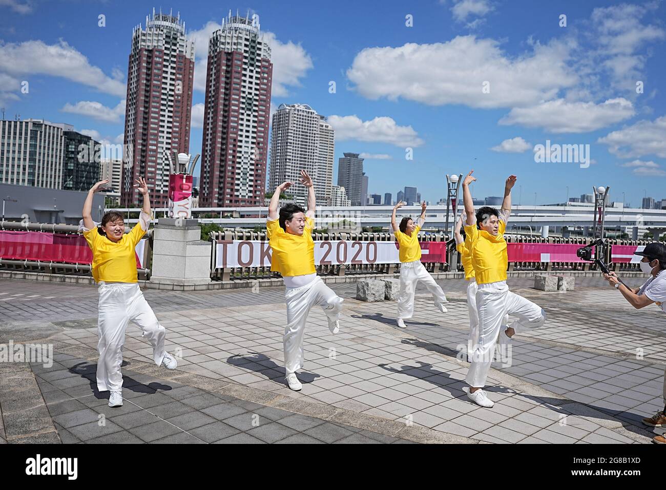 Tokio, Giappone. 19 luglio 2021. Un gruppo balla di fronte a un banner Tokyo 2020 mentre viene girato. Gli anelli si ergono su una zattera nella Baia di Tokyo di fronte al quartiere di Odaiba. Le Olimpiadi di Tokyo 2020 si terranno dal 23 luglio 2021 all'8 agosto 2021. Credit: Michael Kappeler/dpa/Alamy Live News Foto Stock