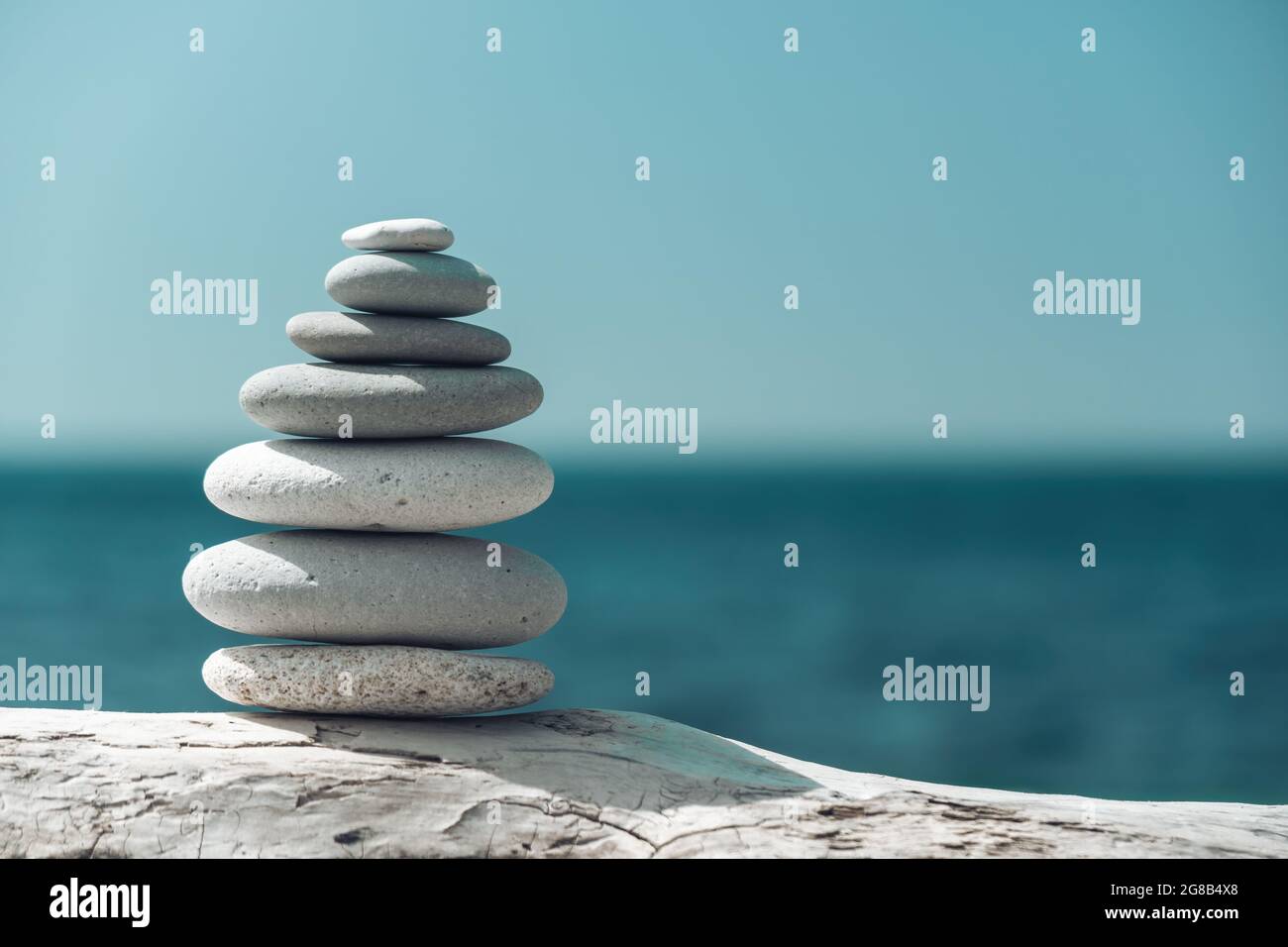 Equilibrata piramide di ciottoli sulla spiaggia in una giornata di sole. Abstract Sea bokeh sullo sfondo. Messa a fuoco selettiva. Pietre Zen sulla spiaggia di mare, meditazione Foto Stock
