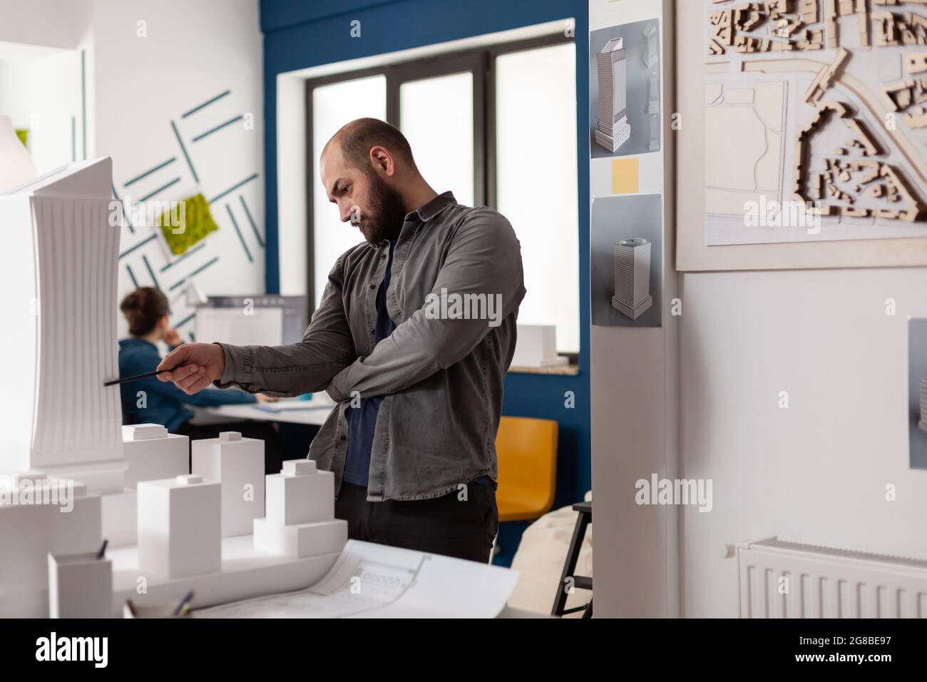 Uomo con professione di architetto sul posto di lavoro che guarda al progetto industriale per la costruzione di maquette modello. Lavoratore caucasico che ispeziona il piano di layout della costruzione sul tavolo per lo schizzo della struttura Foto Stock