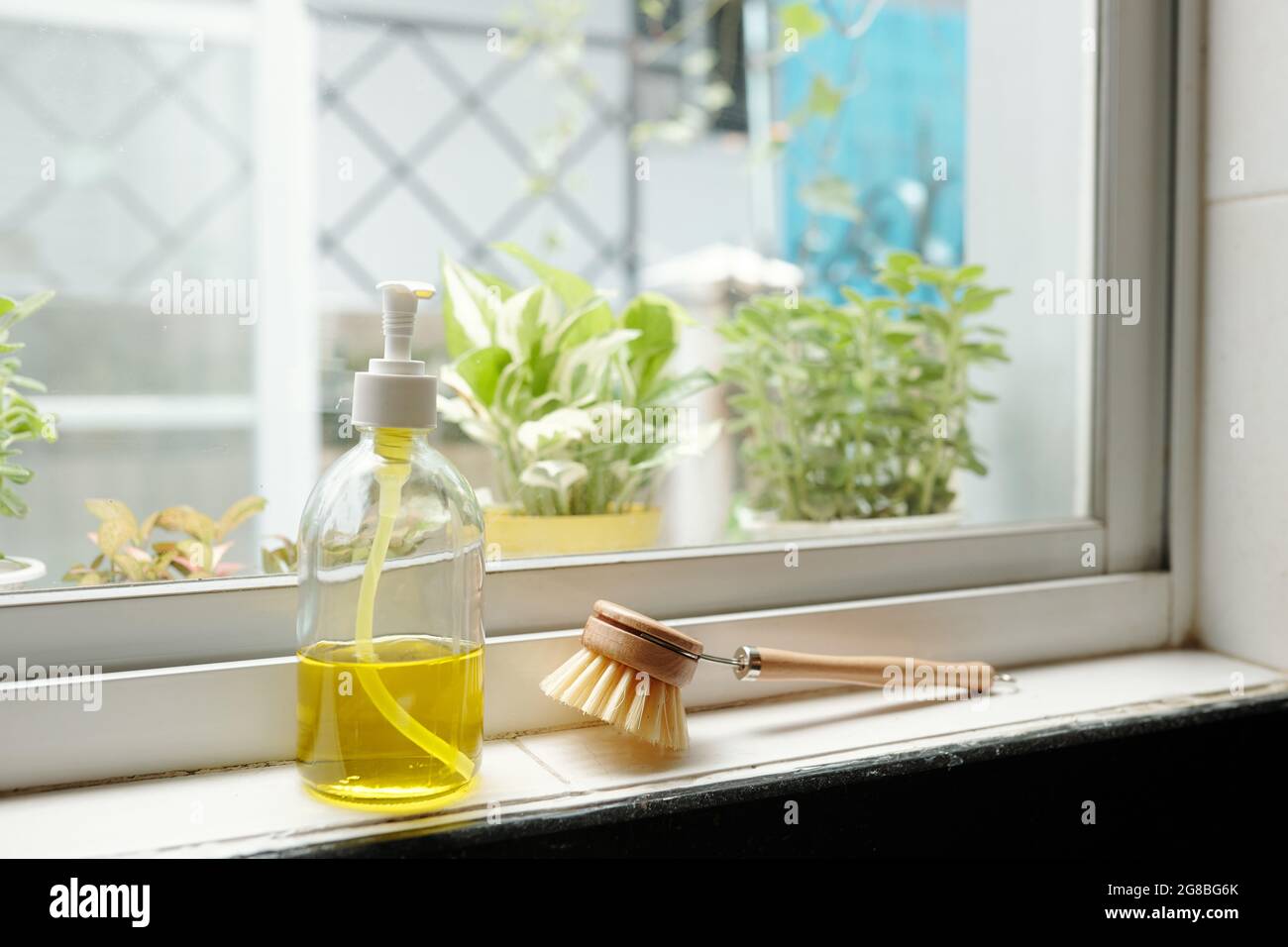 Bottiglia di sapone giallo e spazzola sul davanzale in cucina Foto Stock