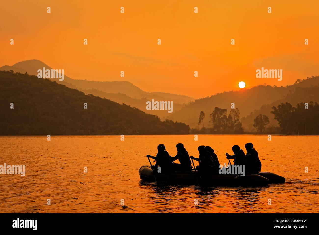 Gruppo di soldati aiutano a filare barca a bersaglio al crepuscolo, montagna e sole in background. Foto Stock