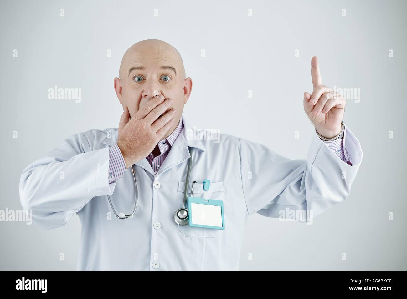 Ritratto di medico sorpreso maturo alzando il dito e chiuse la bocca con la mano cercando di prestare attenzione su di lui Foto Stock