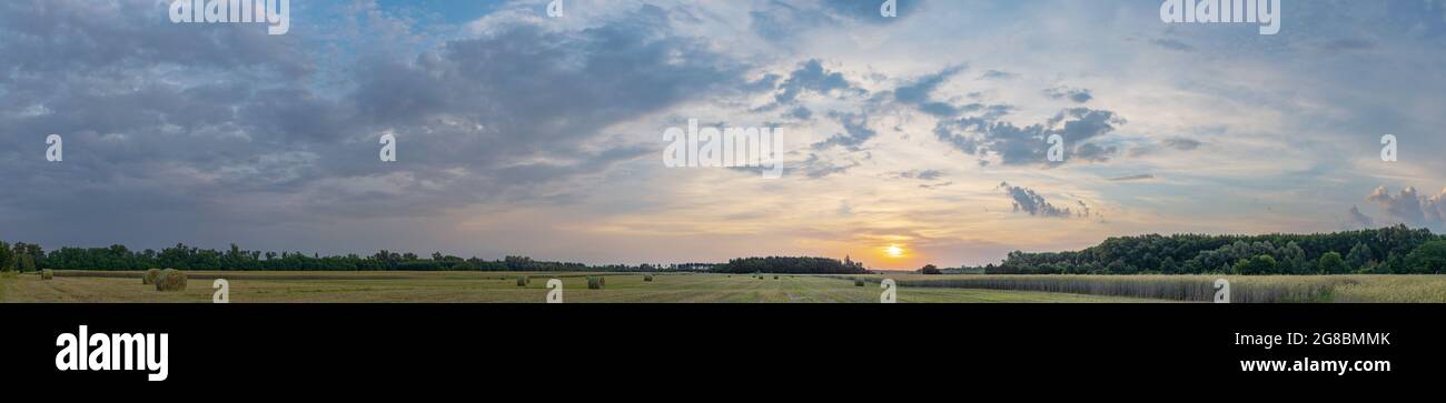 Un rotolo di fieno in campo all'alba con nubi incredibilmente belle. Foto Stock